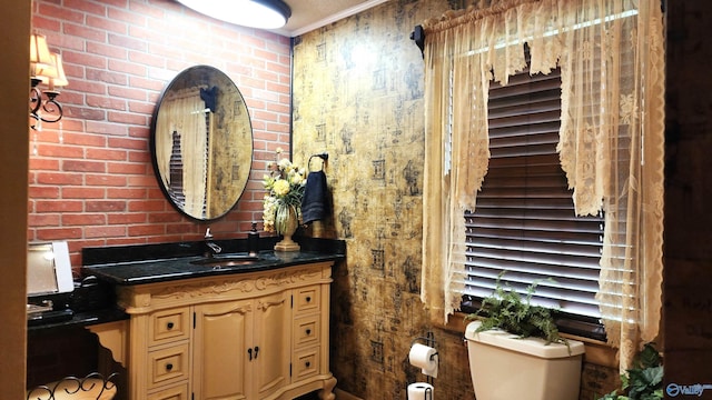 bathroom featuring vanity, brick wall, and toilet