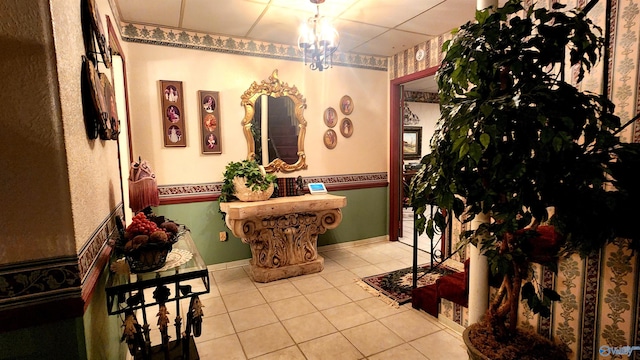 corridor with light tile patterned floors, an inviting chandelier, and a drop ceiling