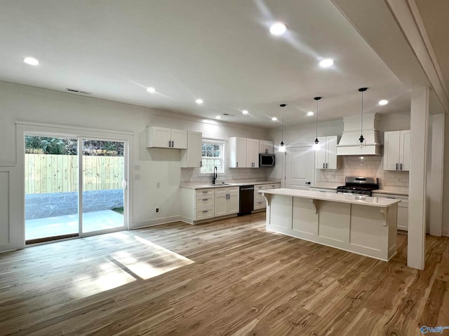 kitchen with white cabinetry, light hardwood / wood-style flooring, stainless steel appliances, decorative light fixtures, and a center island