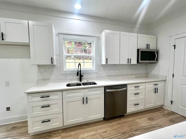 kitchen featuring appliances with stainless steel finishes, sink, backsplash, light hardwood / wood-style floors, and white cabinets