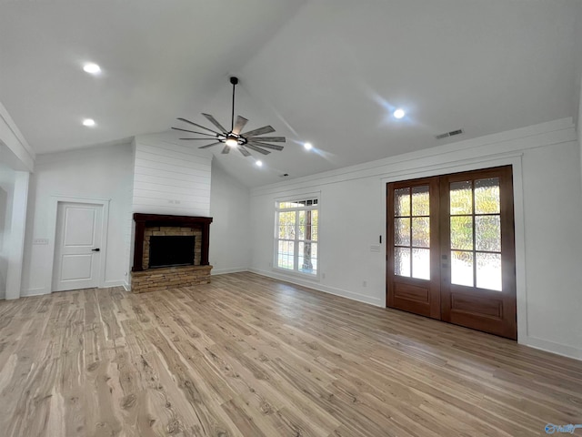 unfurnished living room featuring ceiling fan, vaulted ceiling, light hardwood / wood-style flooring, a fireplace, and french doors