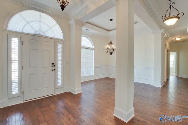 entrance foyer with crown molding, dark wood finished floors, ornate columns, and an inviting chandelier