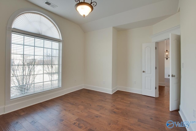 spare room with vaulted ceiling, dark wood-style flooring, visible vents, and baseboards