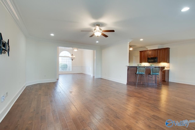 unfurnished living room with ceiling fan with notable chandelier, dark wood-style flooring, baseboards, and crown molding