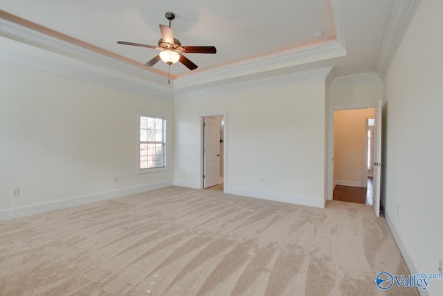 empty room with ceiling fan, light colored carpet, baseboards, a tray ceiling, and crown molding