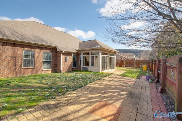 rear view of property with brick siding, a yard, a sunroom, a patio area, and a fenced backyard