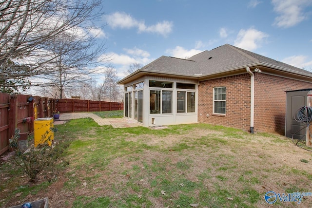 rear view of house featuring a sunroom, a fenced backyard, a yard, and brick siding