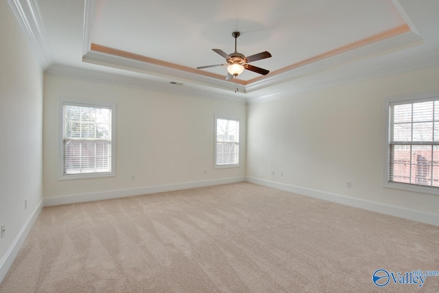 empty room with baseboards, a tray ceiling, crown molding, and light colored carpet