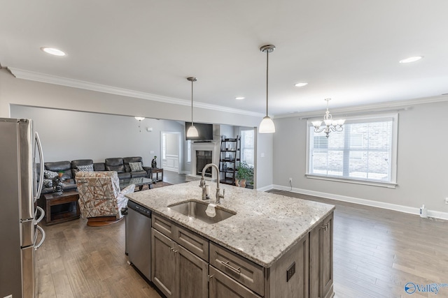 kitchen with sink, decorative light fixtures, appliances with stainless steel finishes, an island with sink, and light stone countertops