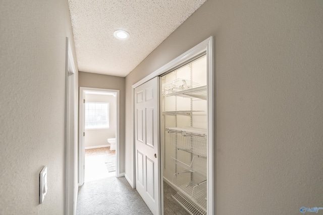 corridor featuring a textured ceiling, baseboards, carpet flooring, and a textured wall