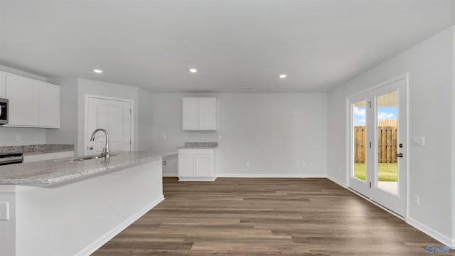 kitchen featuring sink, hardwood / wood-style floors, light stone countertops, a kitchen island with sink, and white cabinets