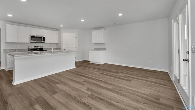 kitchen with white cabinetry, stainless steel appliances, a kitchen island with sink, and light hardwood / wood-style flooring