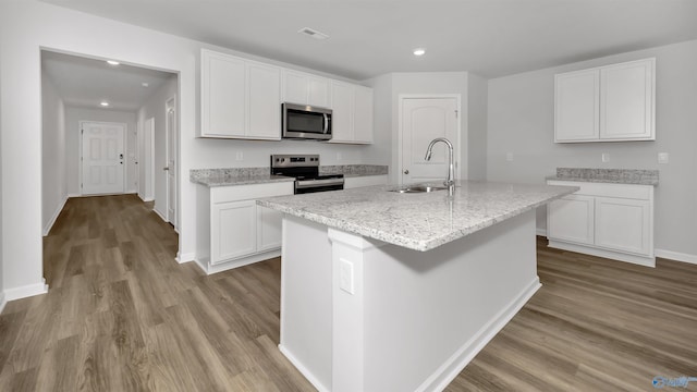 kitchen with appliances with stainless steel finishes, white cabinetry, an island with sink, sink, and light stone counters