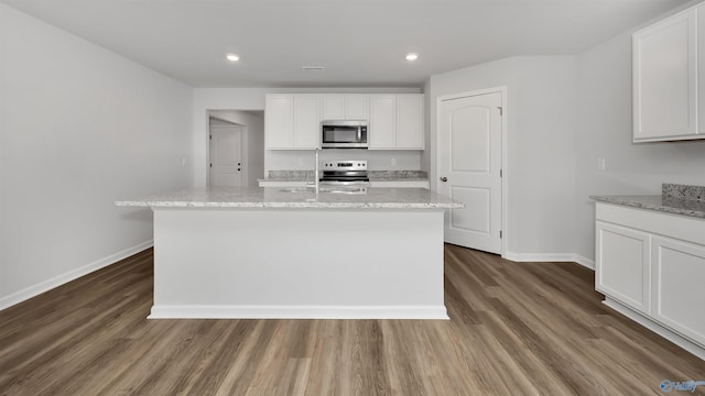 kitchen with stainless steel appliances, white cabinetry, a kitchen island with sink, and light stone counters