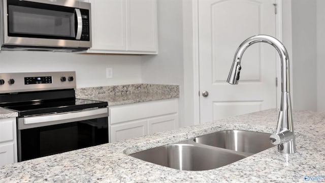 kitchen with white cabinetry, sink, light stone counters, and stainless steel appliances