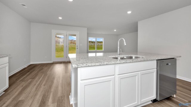 kitchen featuring dishwasher, an island with sink, sink, white cabinets, and light stone counters