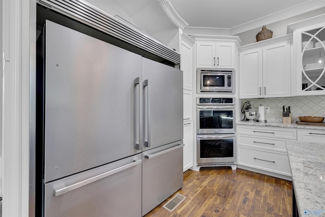 kitchen with dark hardwood / wood-style floors, light stone countertops, built in appliances, tasteful backsplash, and ornamental molding