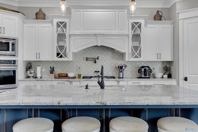 kitchen featuring a kitchen island with sink, stainless steel appliances, light stone countertops, a kitchen breakfast bar, and pendant lighting