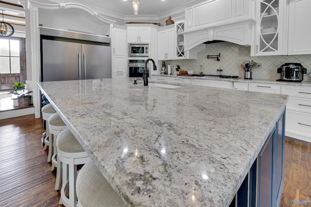 kitchen with dark wood-type flooring, built in appliances, sink, tasteful backsplash, and ornamental molding