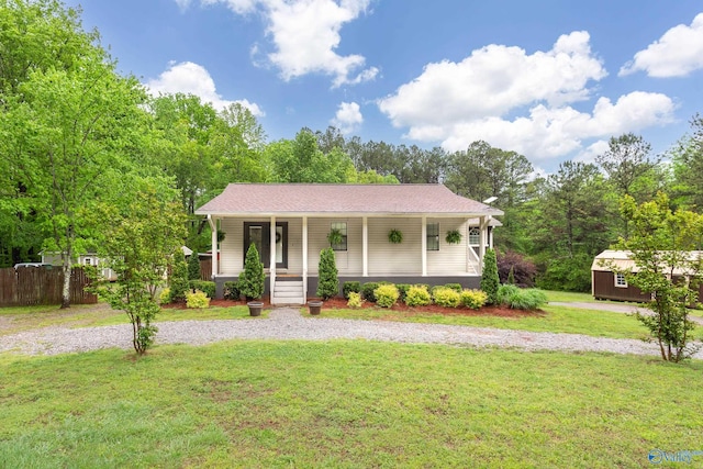 view of front of property featuring a porch, a front lawn, an outbuilding, a storage unit, and fence