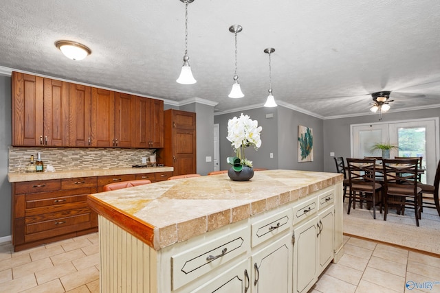 kitchen featuring decorative backsplash, light tile patterned floors, a kitchen island, a ceiling fan, and crown molding