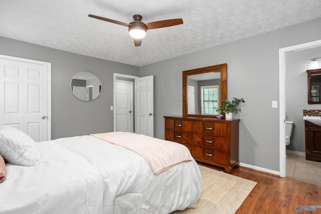 bedroom featuring a textured ceiling, baseboards, wood finished floors, a ceiling fan, and ensuite bath