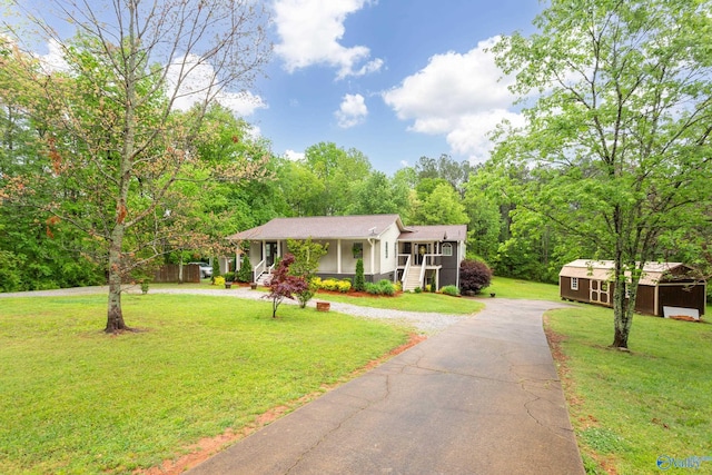 view of front facade featuring aphalt driveway, a porch, a front lawn, and an outbuilding