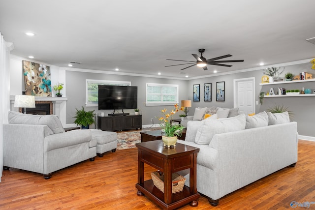 living area with recessed lighting, light wood-style floors, ornamental molding, a glass covered fireplace, and a ceiling fan