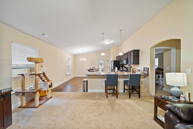 kitchen with vaulted ceiling, a breakfast bar, decorative light fixtures, light stone counters, and light carpet