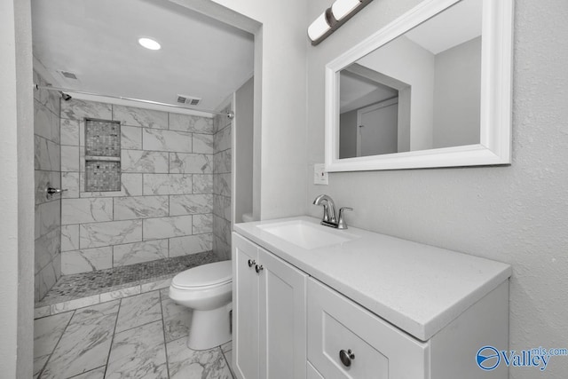 bathroom featuring vanity, a tile shower, and toilet