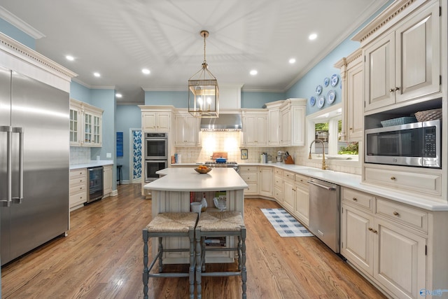 kitchen with a kitchen island, appliances with stainless steel finishes, wine cooler, a kitchen bar, and wall chimney range hood