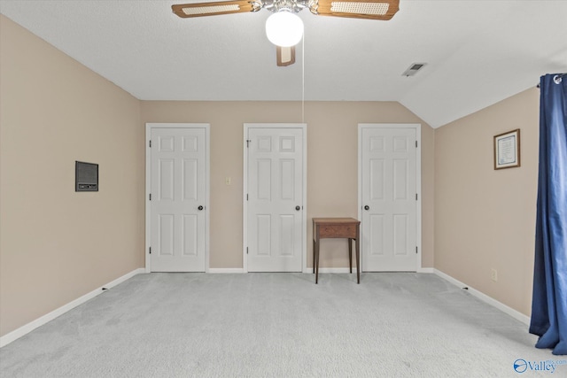 unfurnished bedroom with two closets, ceiling fan, a textured ceiling, light colored carpet, and vaulted ceiling