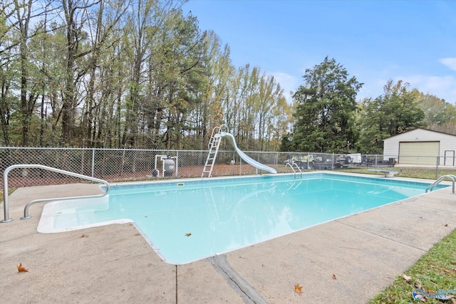 view of swimming pool with a water slide, an outbuilding, and a diving board