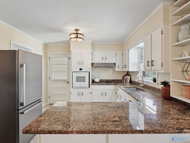 kitchen featuring white cabinets, white oven, stainless steel refrigerator, and sink