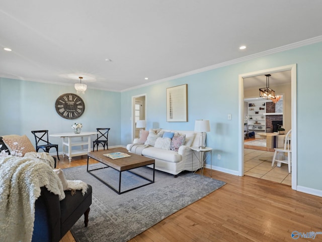 living room featuring a brick fireplace, hardwood / wood-style floors, ornamental molding, and a notable chandelier