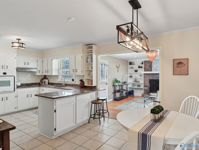 kitchen with pendant lighting, white cabinets, oven, and a fireplace