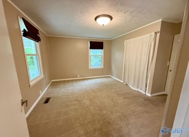 empty room with carpet flooring, crown molding, visible vents, baseboards, and a textured ceiling