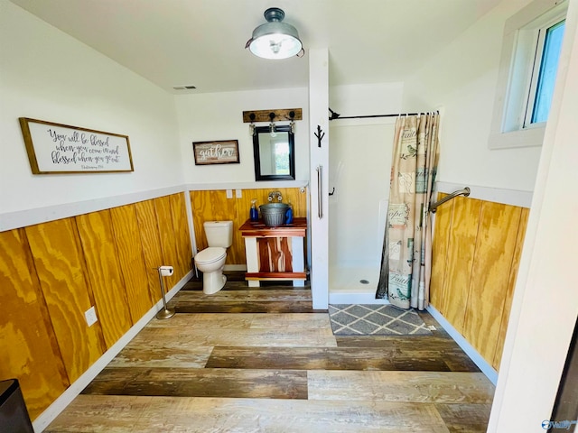 bathroom featuring toilet, wood-type flooring, curtained shower, and wooden walls