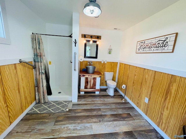 bathroom with toilet, wooden walls, a shower with shower curtain, and hardwood / wood-style floors