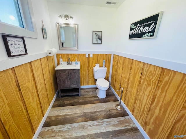 bathroom featuring toilet, wood walls, hardwood / wood-style floors, and vanity