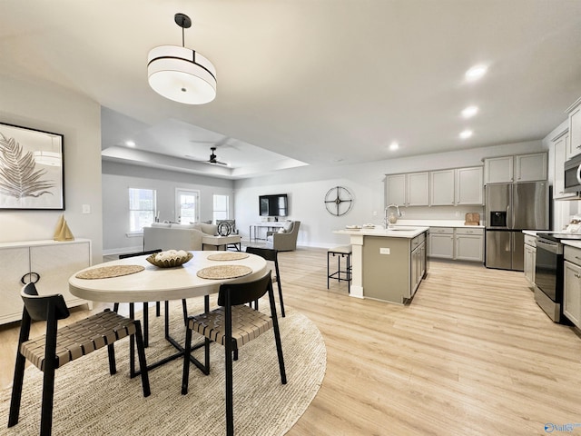 dining room with baseboards, ceiling fan, a tray ceiling, recessed lighting, and light wood-style flooring