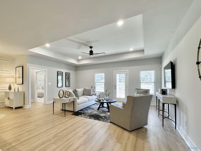 living area featuring baseboards, ceiling fan, light wood-type flooring, a tray ceiling, and recessed lighting