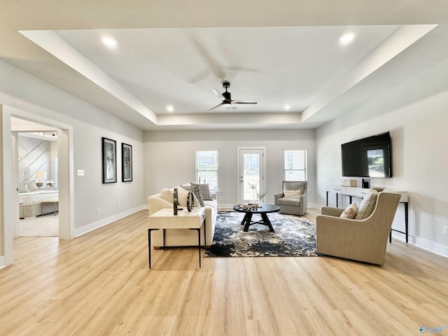 living room with light wood finished floors, baseboards, and a tray ceiling