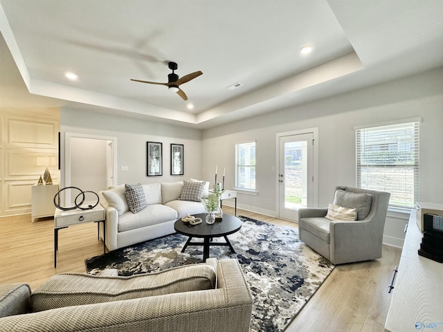 living area with a wealth of natural light, light wood-type flooring, a raised ceiling, and recessed lighting