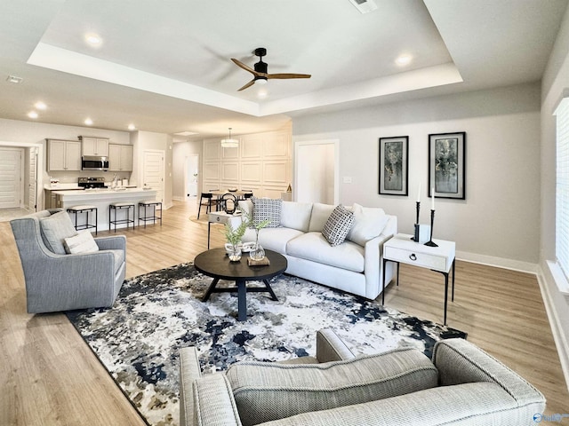 living area featuring light wood-type flooring, a tray ceiling, and baseboards