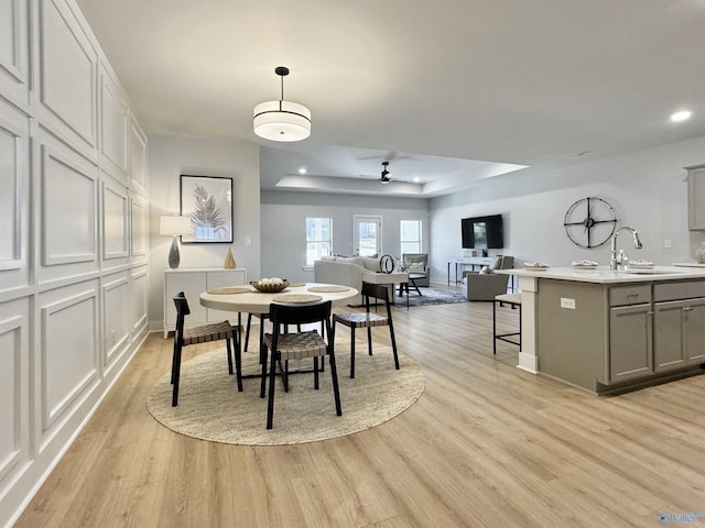 dining room featuring light wood finished floors, baseboards, recessed lighting, a raised ceiling, and a ceiling fan