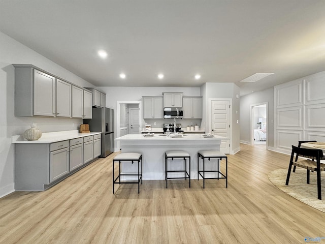 kitchen with light wood-style flooring, gray cabinets, recessed lighting, appliances with stainless steel finishes, and a breakfast bar area