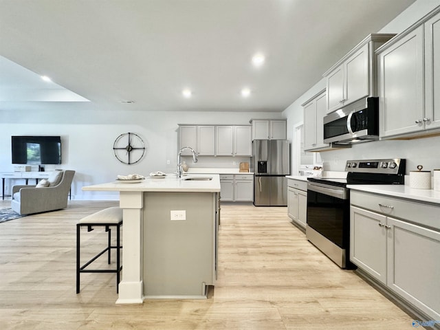 kitchen with open floor plan, a breakfast bar area, light wood-type flooring, appliances with stainless steel finishes, and a sink