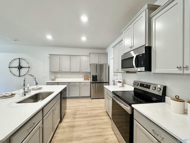 kitchen featuring light wood-style flooring, gray cabinets, a sink, appliances with stainless steel finishes, and light countertops