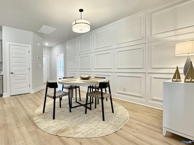 dining space featuring a decorative wall, light wood-style flooring, and baseboards